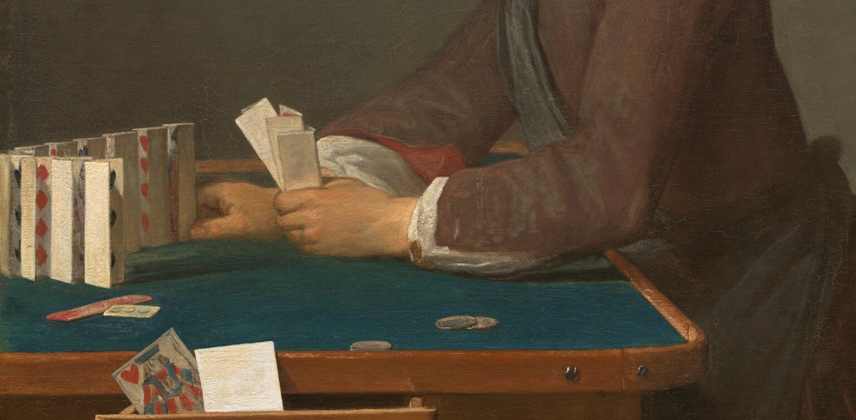 Two arms holding three playing cards with one hand while using the other to arrange a standing card next to ten other playing cards standing on top of a green card table