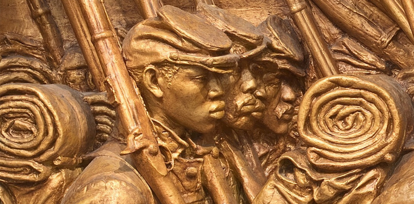 Four African American Civil War soldiers in uniform, marching in formation with bayonets on their right shoulders, backpacks, and hats on.