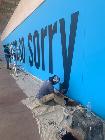 Two men painting SORRY onto the window covering of the East Building