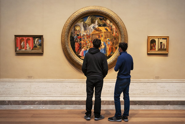 Two people standing in front of a round painting with two smaller painting on either side.