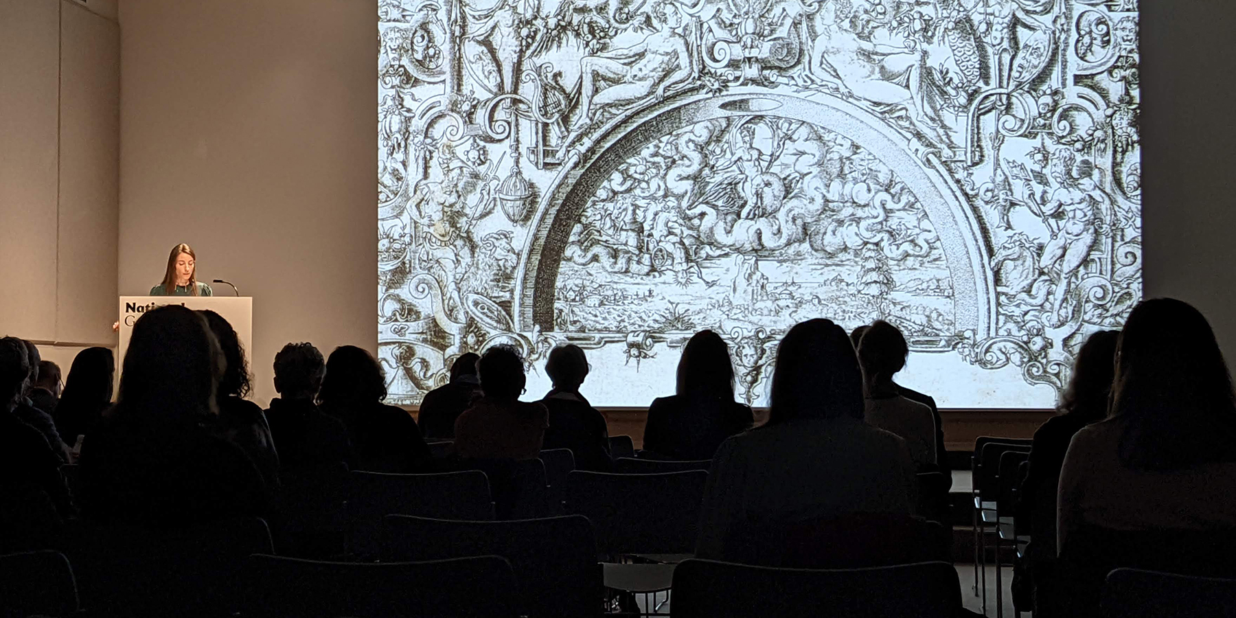 a masked person is looking over a large book with prints, with other prints displayed on a counter surrounding the room