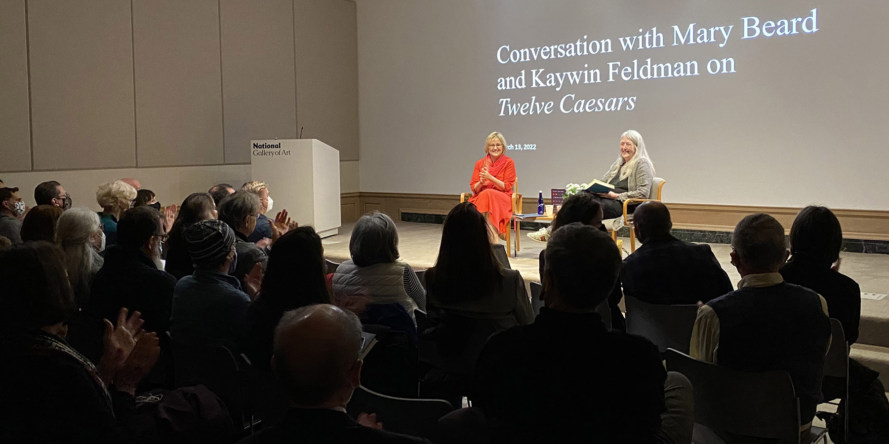 A detail of a painting with a seated woman to the left holding a sleeping puppy, looking at the viewer, while a younger girl faces away from the viewer and stares through bars looking at the smoke of a train