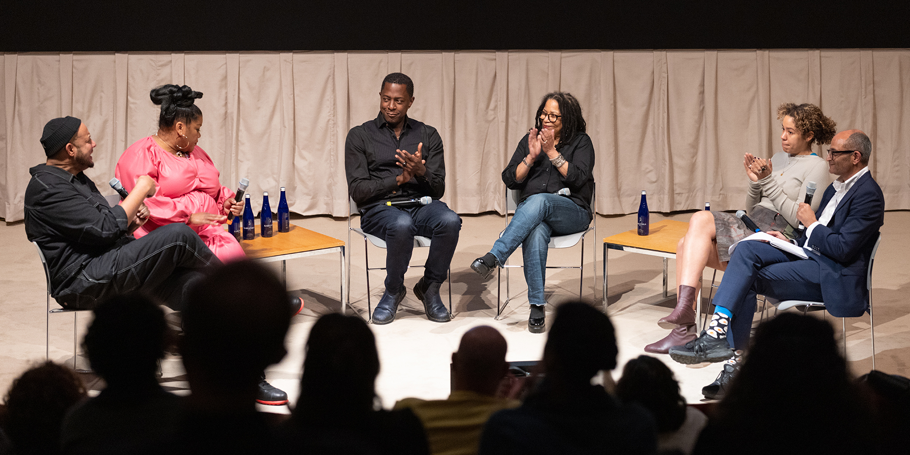a masked person is looking over a large book with prints, with other prints displayed on a counter surrounding the room