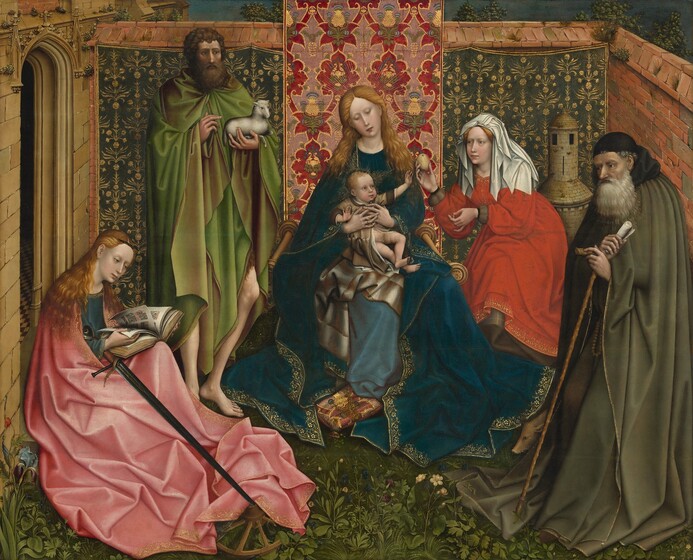 Three women, two men, and an infant are gathered within a walled garden that extends off a building, its façade visible to the left, in this horizontal painting. The women have pale white skin and the men have olive-toned complexions. The men and women all wear voluminous, flowing robes and garments in lapis blue, ruby red, rose pink, olive or spring green. At the center a woman, Mary, supports a partially nude and squirming infant on her lap. Mary has wavy blond hair and wears a dark blue velvet robe that pools on the ground around her, with a lighter blue dress beneath. She sits on a chair with wooden spindle arms facing forward, toward us. She holds up the infant with interlaced fingers that wrap around his middle, and she inclines her head down and to our left, toward the infant. The child has blond hair, wide open blue eyes, and a chubby, pink-cheeked face. He is wrapped in a long, shimmery gold robe with brown cuffs and collar, which is open over his lower torso and legs. Facing our right, the child reaches with his left arm, palm outward. An array of shimmery, gold painted lines fan out around the heads of Mary and the infant. Just beyond the child’s reach, a woman in a red dress and shoulder-length, white head covering bends toward him and holds out a golden apple or other fruit. To our right, an elderly man has a full gray beard, and he gazes to our left. He leans, semi-stooping, on a walking stick that pins the hem of his garment. He wears a flowing cape in olive green with a black hood bunched across his shoulders, and a black skullcap. At his right foot, a small hog noses out from amid the draped garments. To the left of Mary stands a tall man in a spring-green cape with a gold lining, which hangs around his knees, exposing his lower legs and bare feet. He has bushy brown hair and a full beard. He cradles a small white lamb in his left arm while gesturing toward it with his right. His head is turned to our right, and he gazes off in that direction. Next to him, on the left side of the painting, a pale woman with flowing red hair in a pale pink cape sits on the ground directly in front of an arched doorway leading into the stone building. She sits facing our right, almost in profile. She bends her head toward a large, bound book resting on her lap that has lines of calligraphic writing in black and red. Propped beneath her right arm and projecting outward is a black metal sword that has a heart-shaped top. The sword’s tip touches a wooden wheel that lies on the grass, partially under the woman’s garments. The brick wall behind the group is covered across its width with a green and gold tapestry or cloth with a repeating floral motif. In the center, a vertical woven cloth of red and gold heraldic designs, with blue and green details, extends to the top of the painting, forming a backdrop behind Mary and the child. The ground is covered with green vegetation and a few small, pale yellow flowers blooming at the group’s feet. Over the wall, which is slightly higher than the standing man’s head, a sliver of blue sky and treetops is visible.
